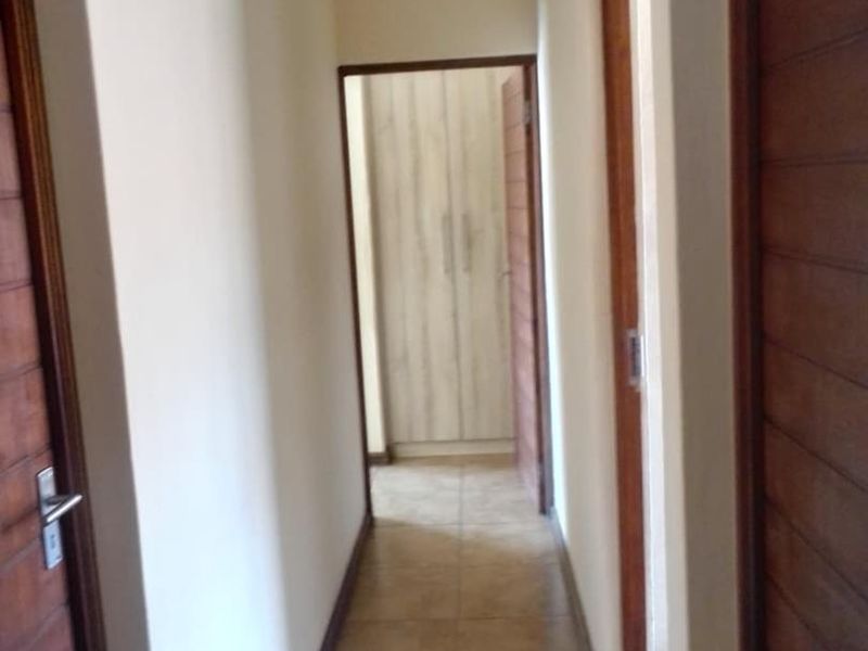 A clean, empty hallway featuring tiled flooring, wooden doors, and built-in storage cupboards at the end of the passage.