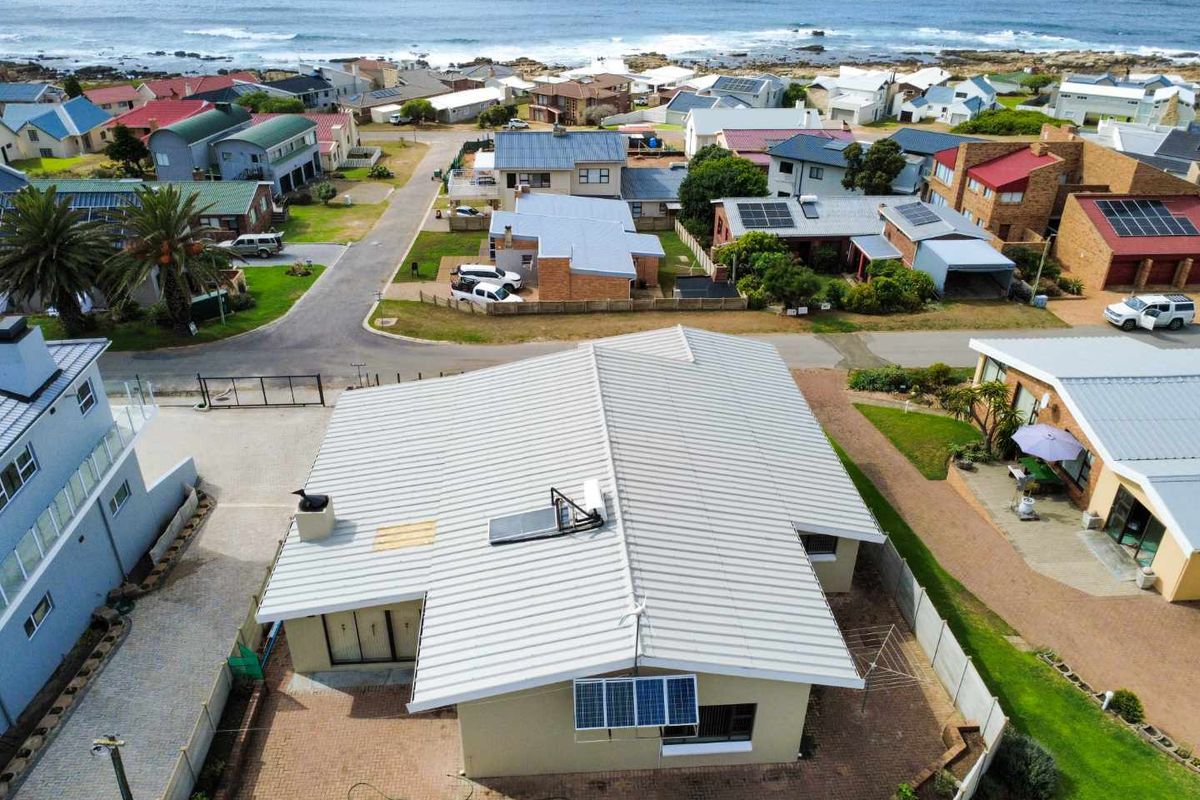 Aerial view of a coastal residential property featuring a metal roof with solar panels and a paved rear courtyard area.