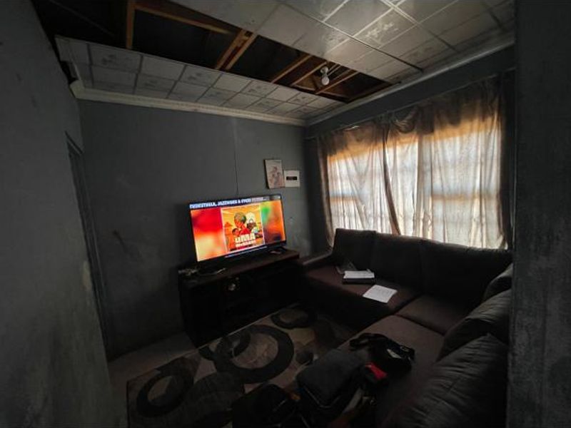 A living room space featuring a drop ceiling with visible damage and missing tiles, requiring repair and cosmetic updates.
