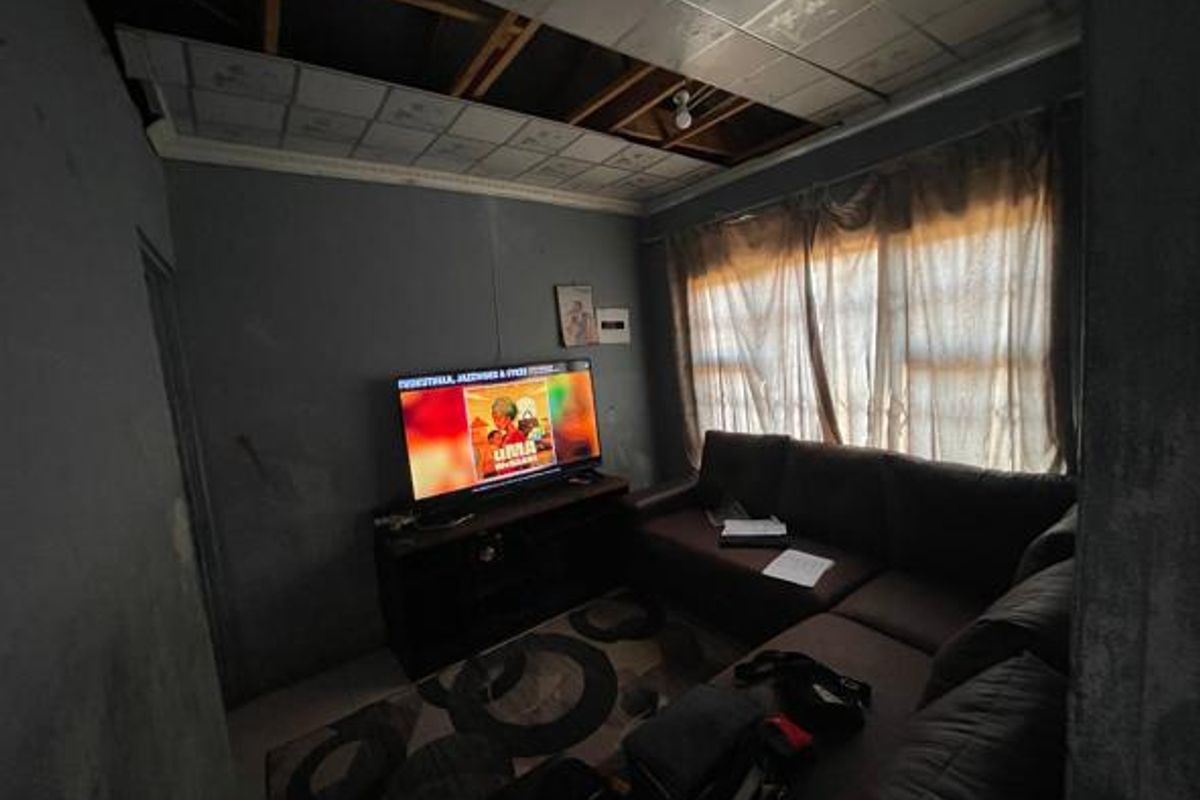 A living room space featuring a drop ceiling with visible damage and missing tiles, requiring repair and cosmetic updates.