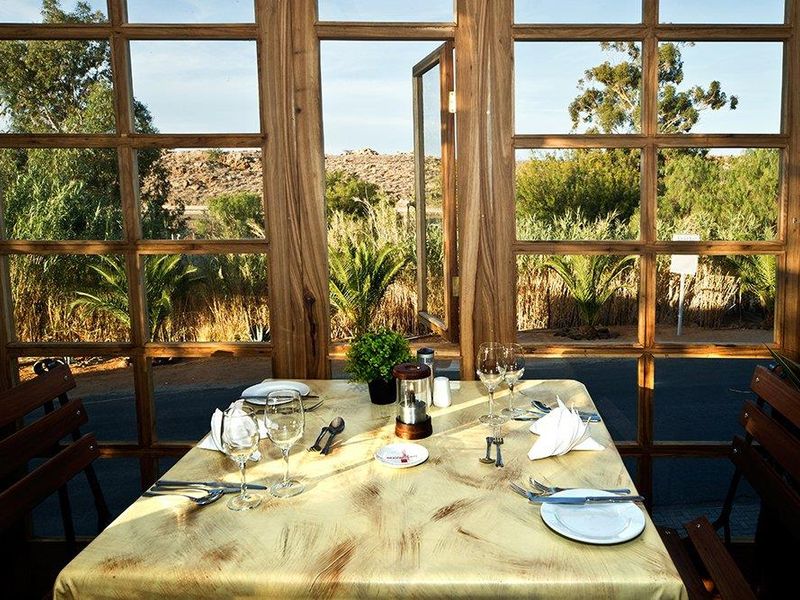 A dining area featuring large timber-framed windows that provide natural light and views of the surrounding landscape.
