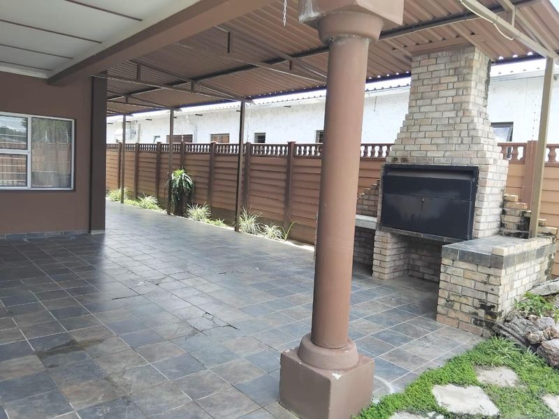 A spacious covered patio featuring a built-in brick braai, tiled flooring, and support columns, ideal for outdoor entertaining.