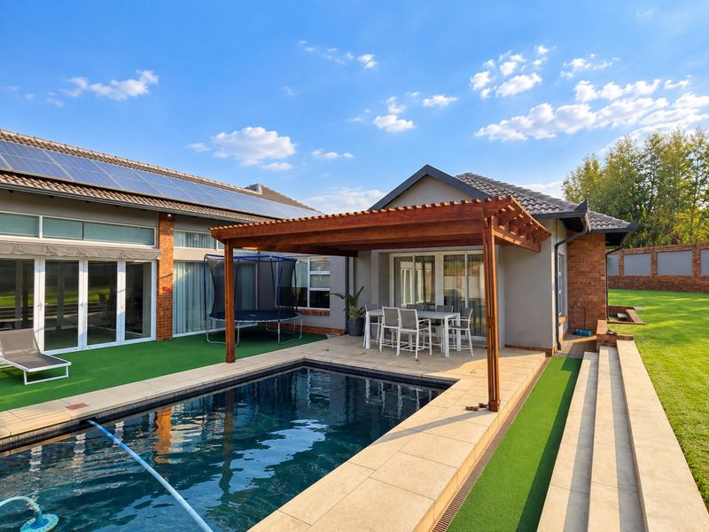 Outdoor entertainment area featuring a swimming pool, wooden pergola, and tiled patio, set against a well-maintained garden and brick-clad house exterior.