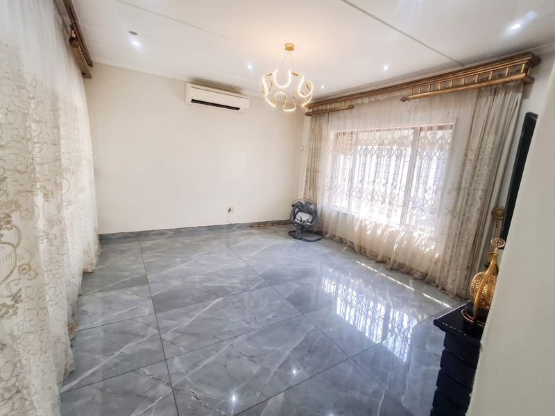 A bright and spacious living area featuring large format grey marble-look floor tiles, modern lighting, and a wall-mounted air conditioning unit.