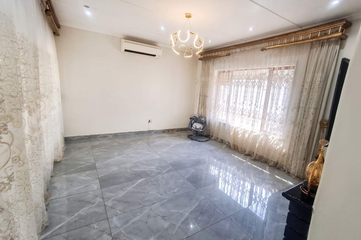 A bright and spacious living area featuring large format grey marble-look floor tiles, modern lighting, and a wall-mounted air conditioning unit.