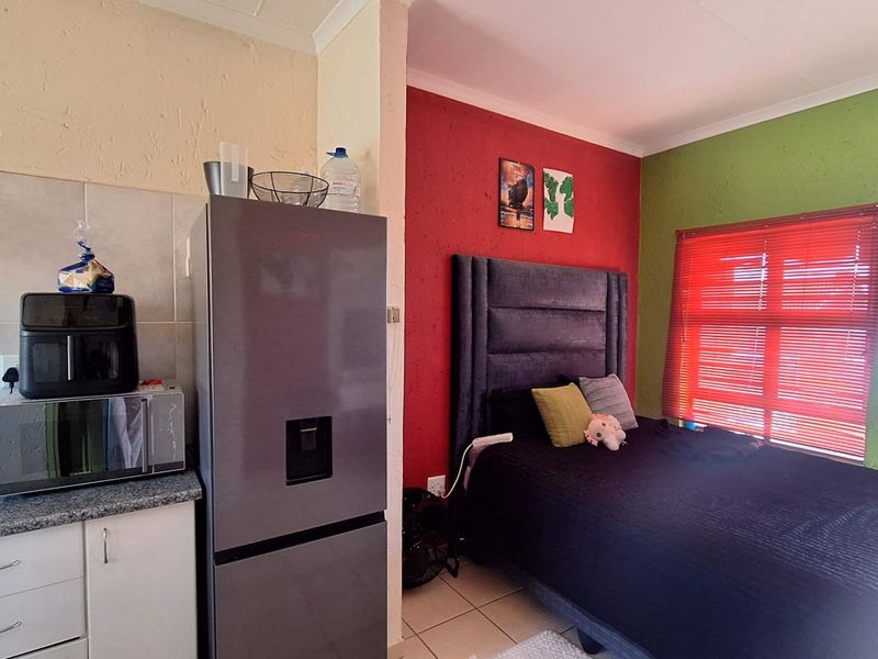 An open-plan studio apartment featuring a compact kitchen area with granite countertops adjacent to a bedroom space with tiled flooring and window blinds.