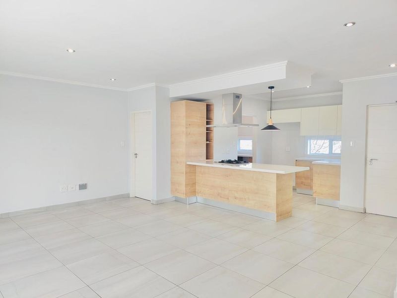 Spacious open-plan living area featuring a modern kitchen with light wood cabinetry, a central island, and neutral tiled flooring throughout.