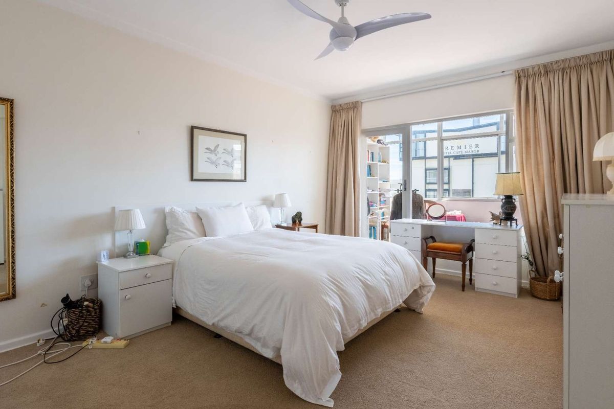 A well-lit bedroom featuring neutral carpet flooring, a ceiling fan, and a sliding glass door providing access to an outdoor balcony area.
