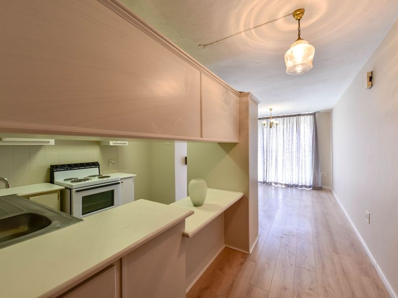 An open-plan living and kitchen area featuring laminate flooring, built-in cabinetry, and a functional kitchen layout with a freestanding stove.