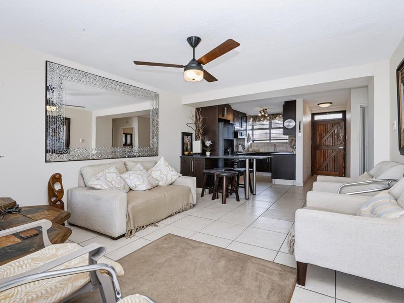 Open plan living and kitchen area featuring tiled flooring, a central ceiling fan, and a functional kitchen layout with dark cabinetry.