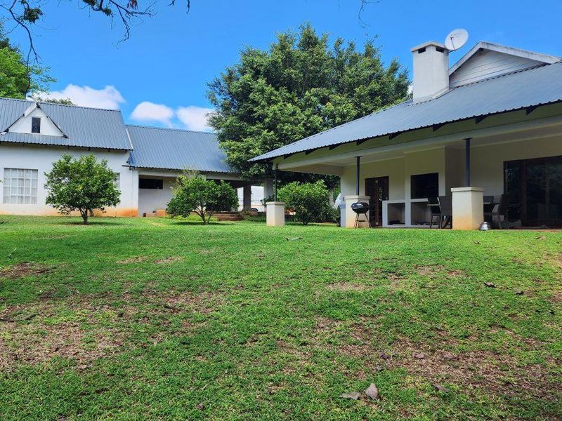 Rear view of the small holding featuring a spacious lawn, covered patio area with a built-in braai, and metal roof structures.