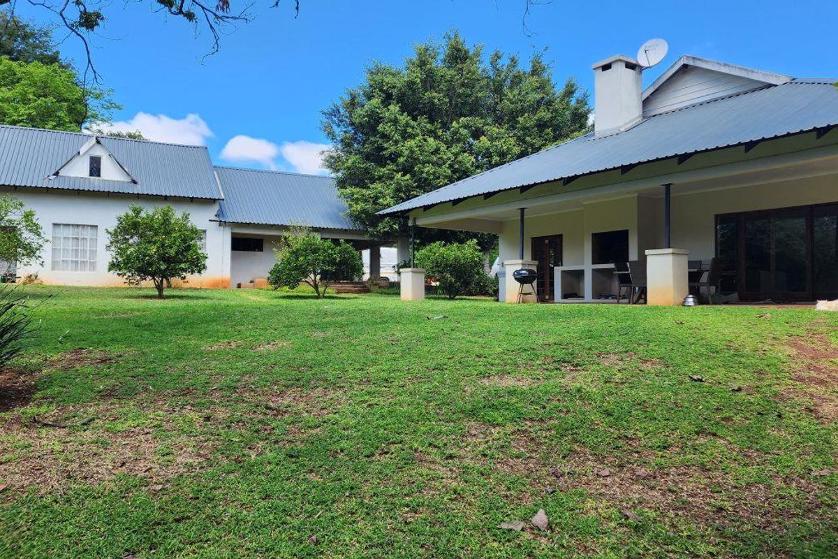 Rear view of the small holding featuring a spacious lawn, covered patio area with a built-in braai, and metal roof structures.