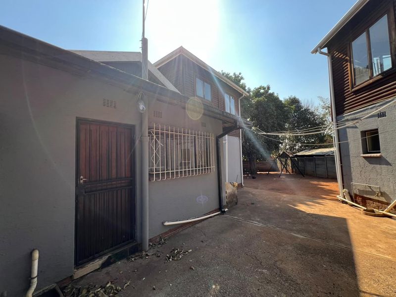 Rear exterior view of the property featuring a concrete driveway, security gates, and timber cladding on the upper level.