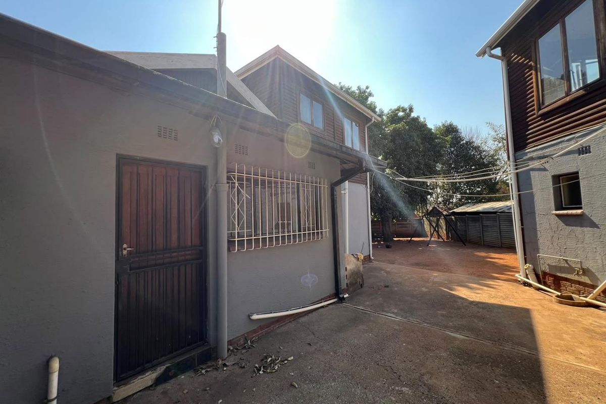 Rear exterior view of the property featuring a concrete driveway, security gates, and timber cladding on the upper level.