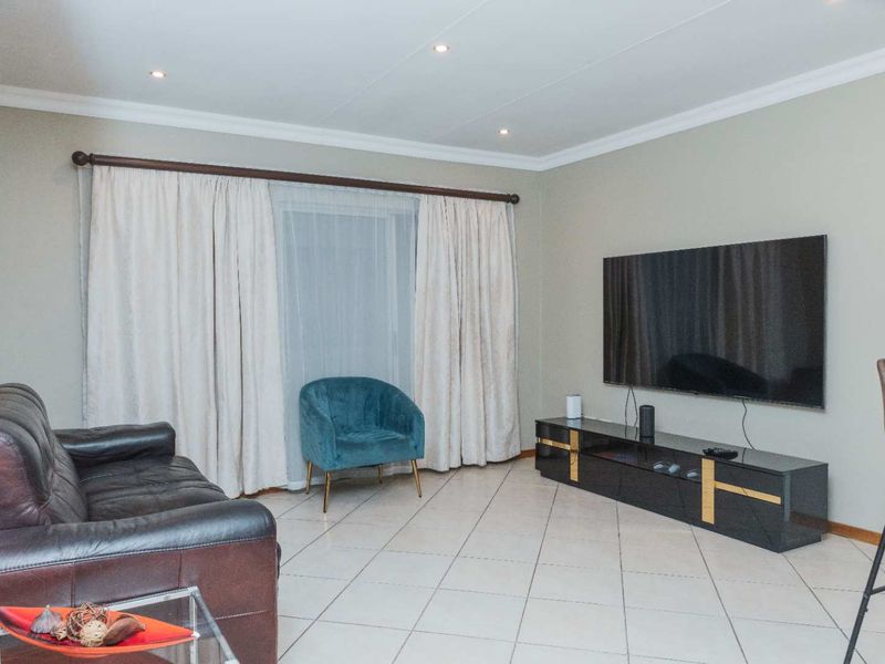 A well-maintained living room featuring neutral tiled flooring, recessed downlighting, and decorative cove cornicing, providing a clean and functional space.
