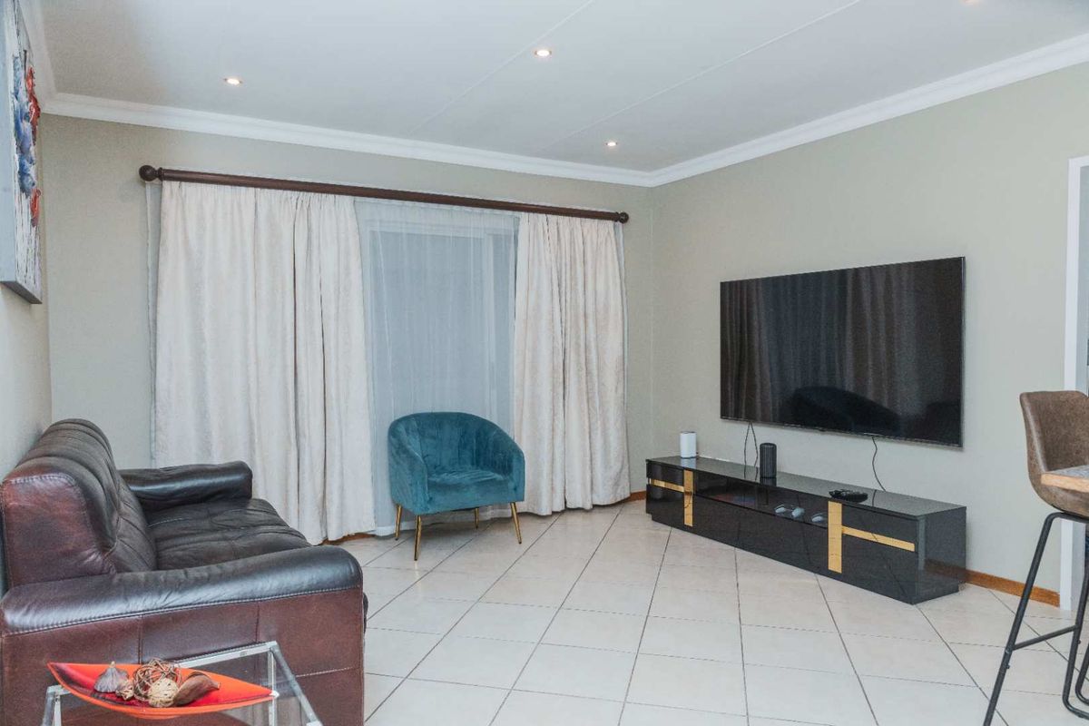 A well-maintained living room featuring neutral tiled flooring, recessed downlighting, and decorative cove cornicing, providing a clean and functional space.