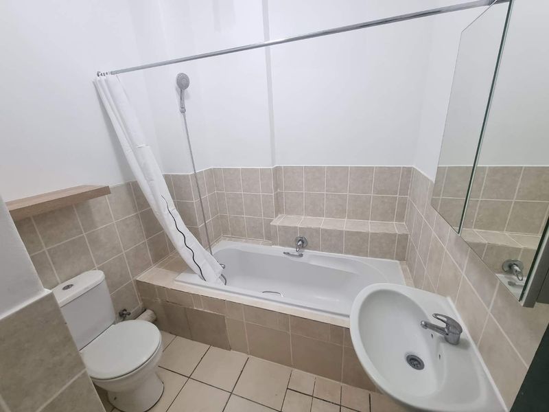 A functional bathroom featuring a built-in bathtub with shower attachment, pedestal washbasin, toilet, and neutral ceramic tiling throughout.