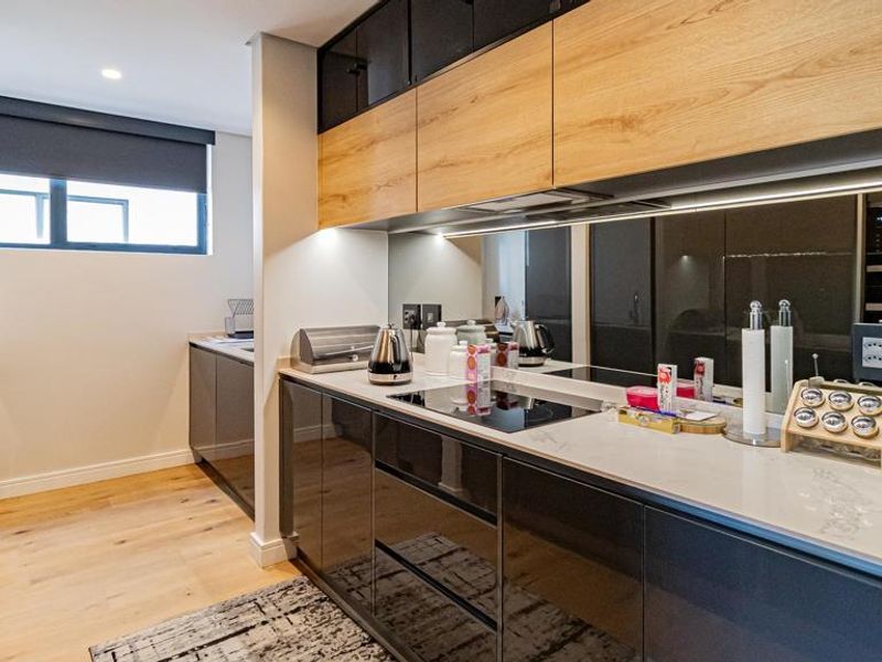 Modern kitchen featuring sleek high-gloss cabinetry, timber flooring, stone countertops, and integrated appliances with a stylish mirrored splashback.