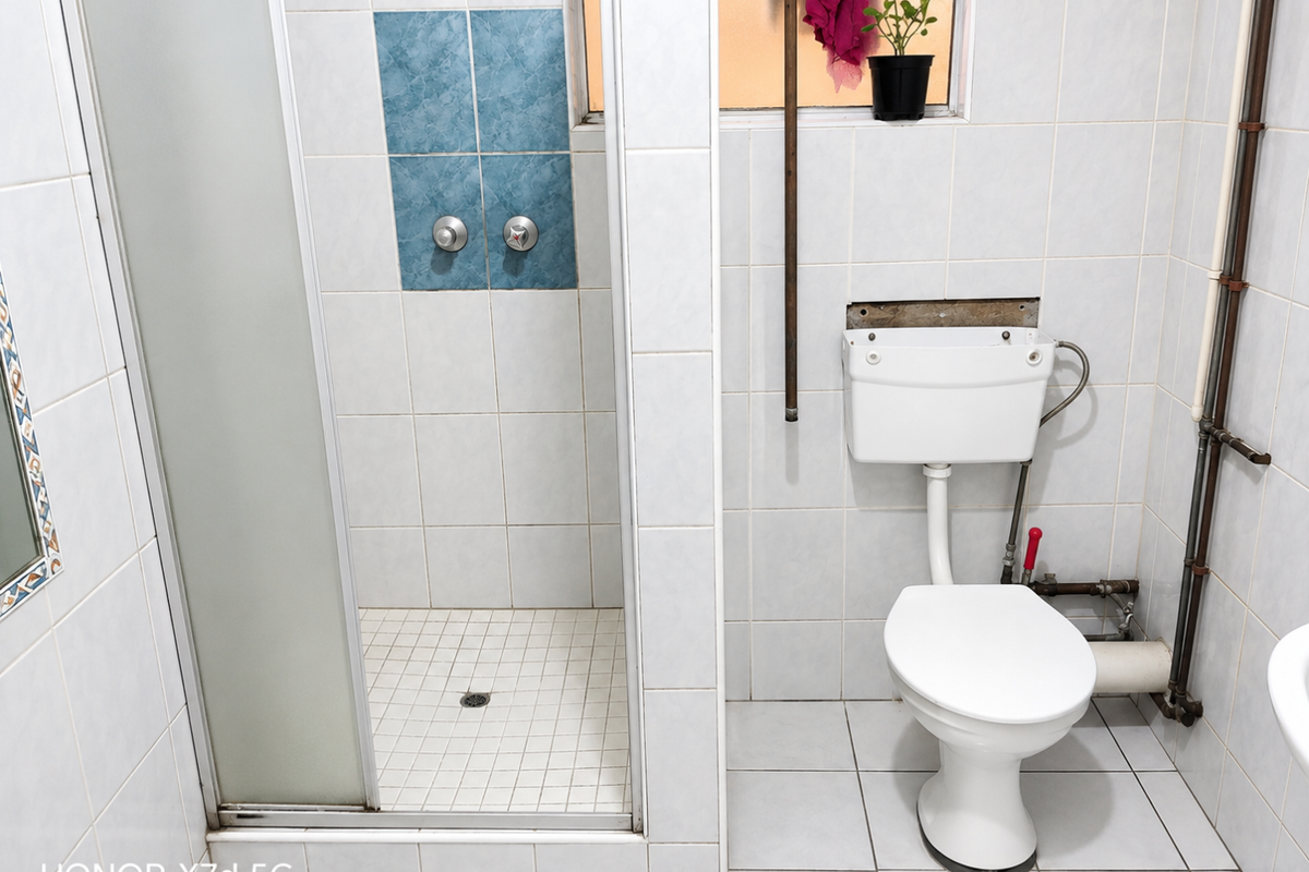 Bathroom featuring a shower enclosure and toilet with exposed plumbing and visible maintenance requirements on the wall finish.