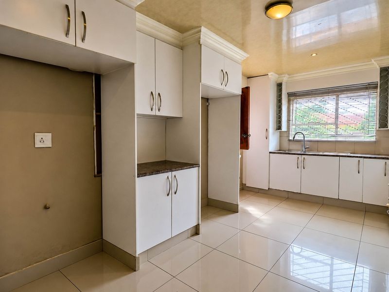 A clean and functional kitchen featuring white built-in cabinetry, laminate countertops, tiled flooring, and a stainless steel sink with a window view.