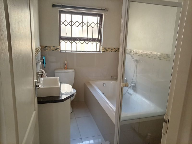 A functional bathroom featuring a built-in bathtub, separate shower enclosure, vanity basin with granite countertop, and decorative mosaic tile accents.