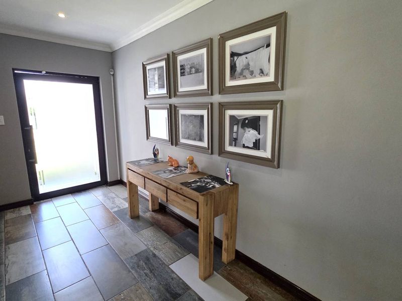 A bright and welcoming entrance hall featuring modern multi-toned tiled flooring, neutral wall finishes, and decorative coving.