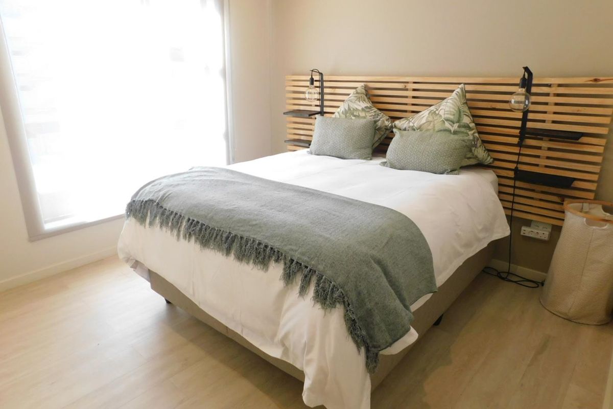 A bright and modern bedroom featuring light wood-look flooring and a custom timber slat headboard with integrated shelving and lighting.
