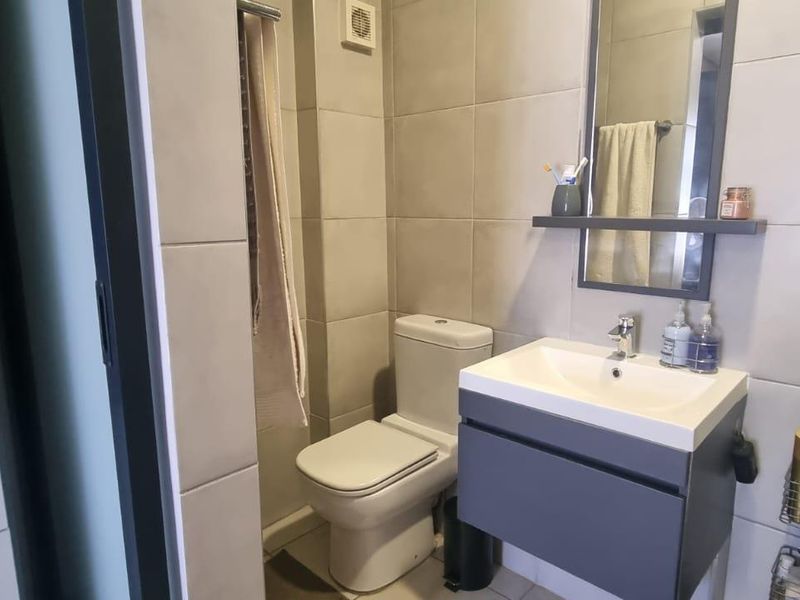 A modern, compact bathroom featuring a wall-mounted vanity with a basin, a toilet, and neutral wall tiling.