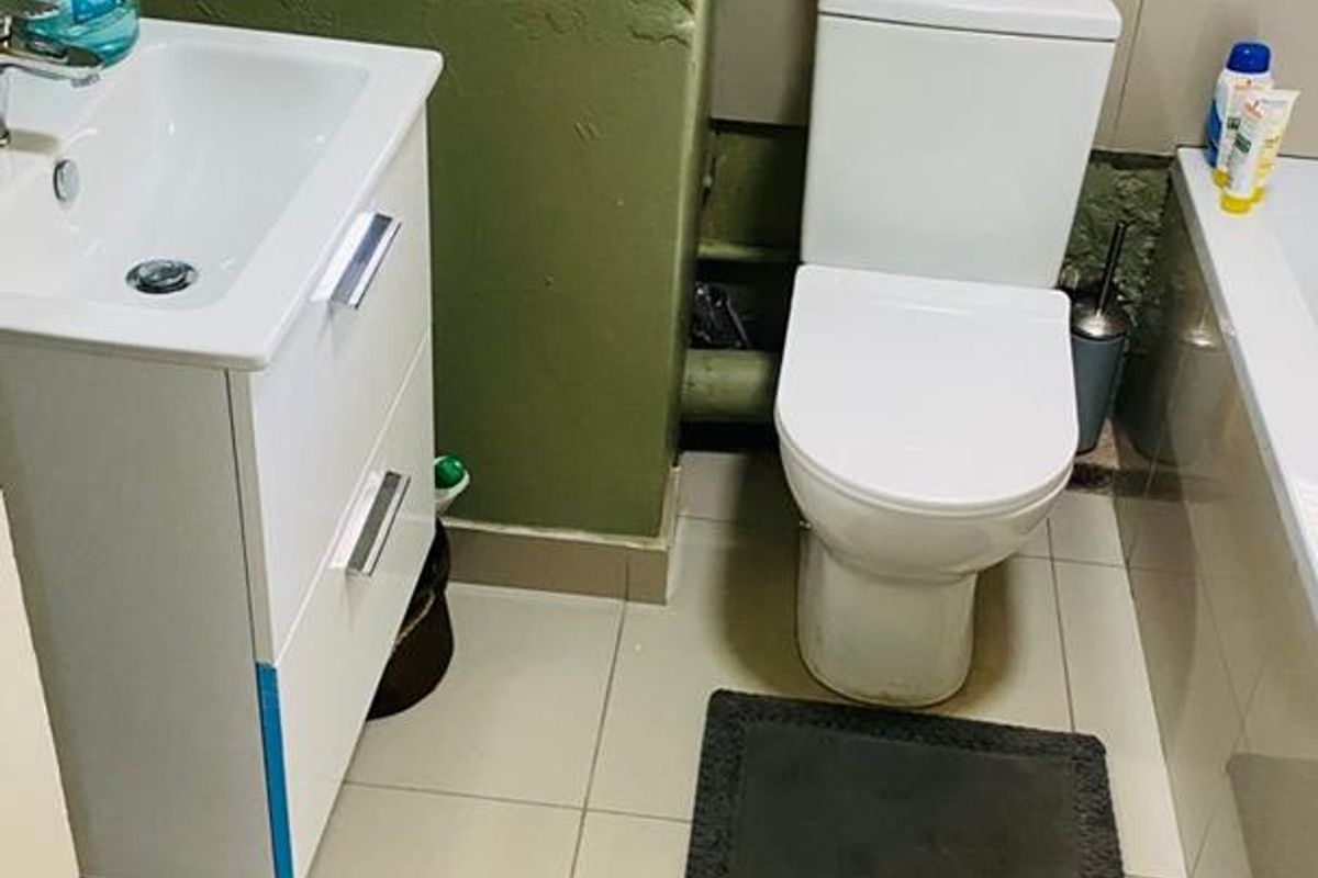 Compact bathroom featuring a wall-mounted vanity, standard toilet, and bathtub with tiled flooring and visible plumbing infrastructure.