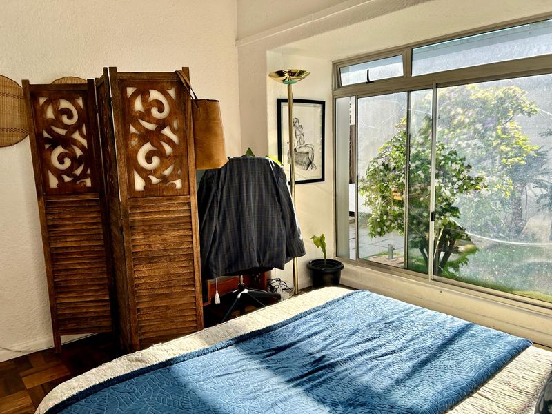 A bedroom featuring classic parquet flooring and a large sliding window that provides natural light and a view of the garden.