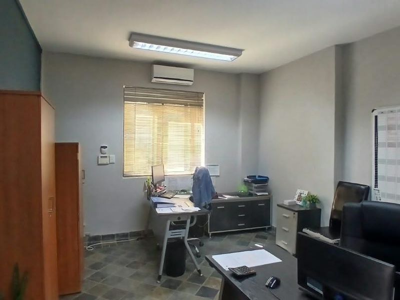 A functional office space featuring tiled flooring, a wall-mounted air conditioning unit, and natural light provided by a window with venetian blinds.