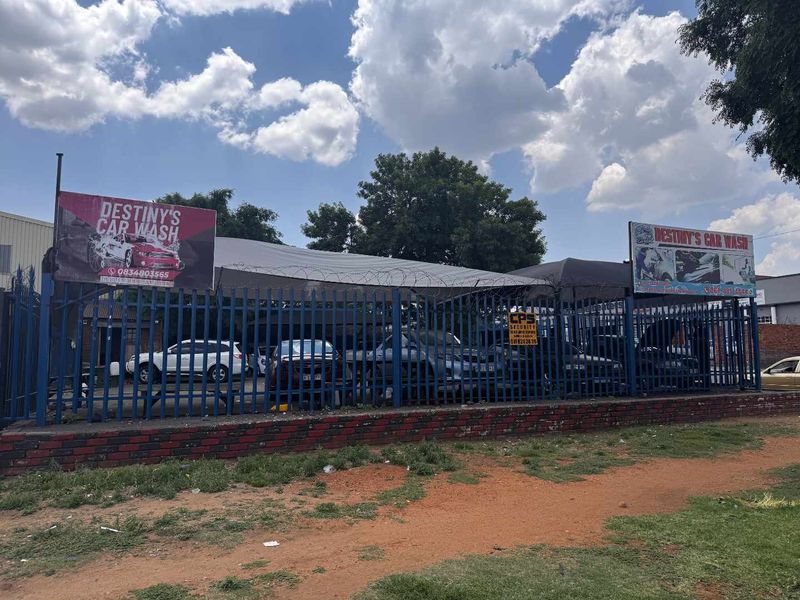 Exterior view of a commercial property featuring a steel palisade fence with razor wire, a shade cloth canopy, and prominent signage for a car wash.