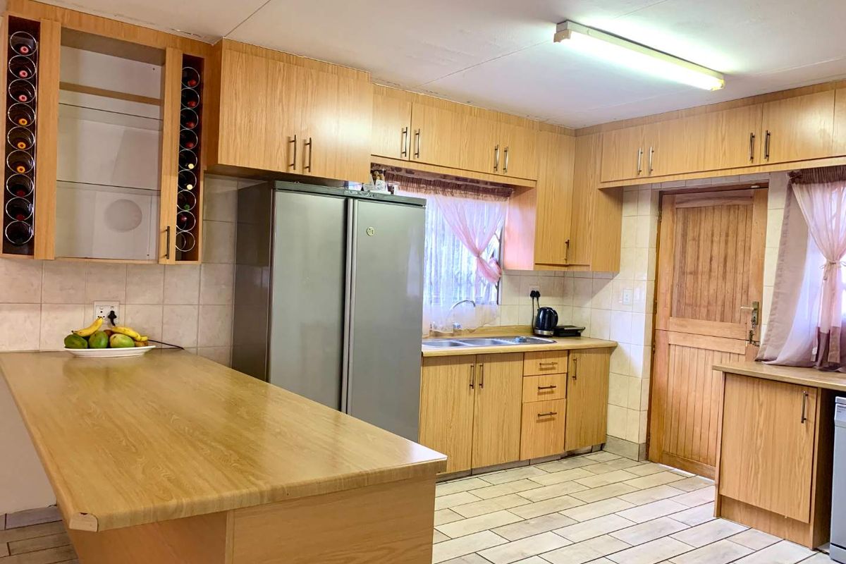 A functional kitchen featuring light wood-look cabinetry, a breakfast bar, tiled flooring, and a double sink with a wooden door leading outdoors.