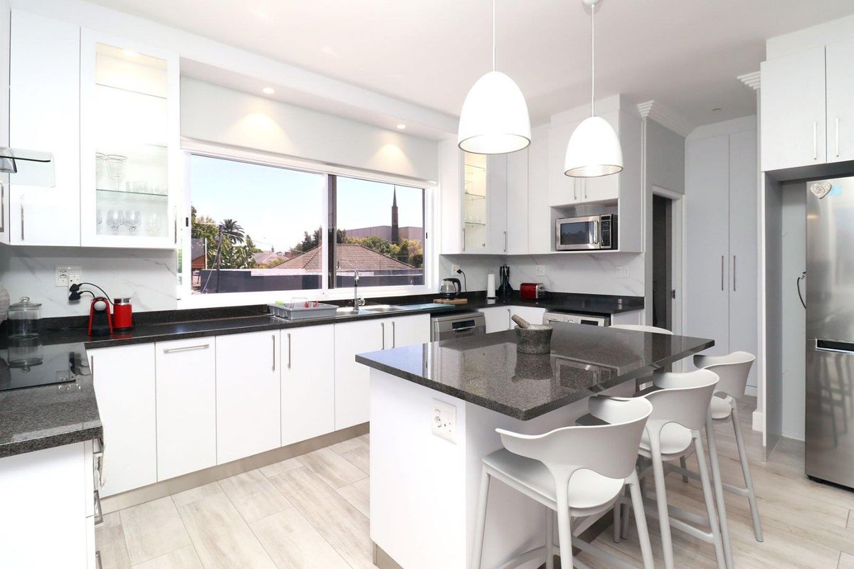 Modern kitchen featuring white cabinetry, dark granite countertops, a central island with breakfast bar seating, and high-quality integrated appliances.