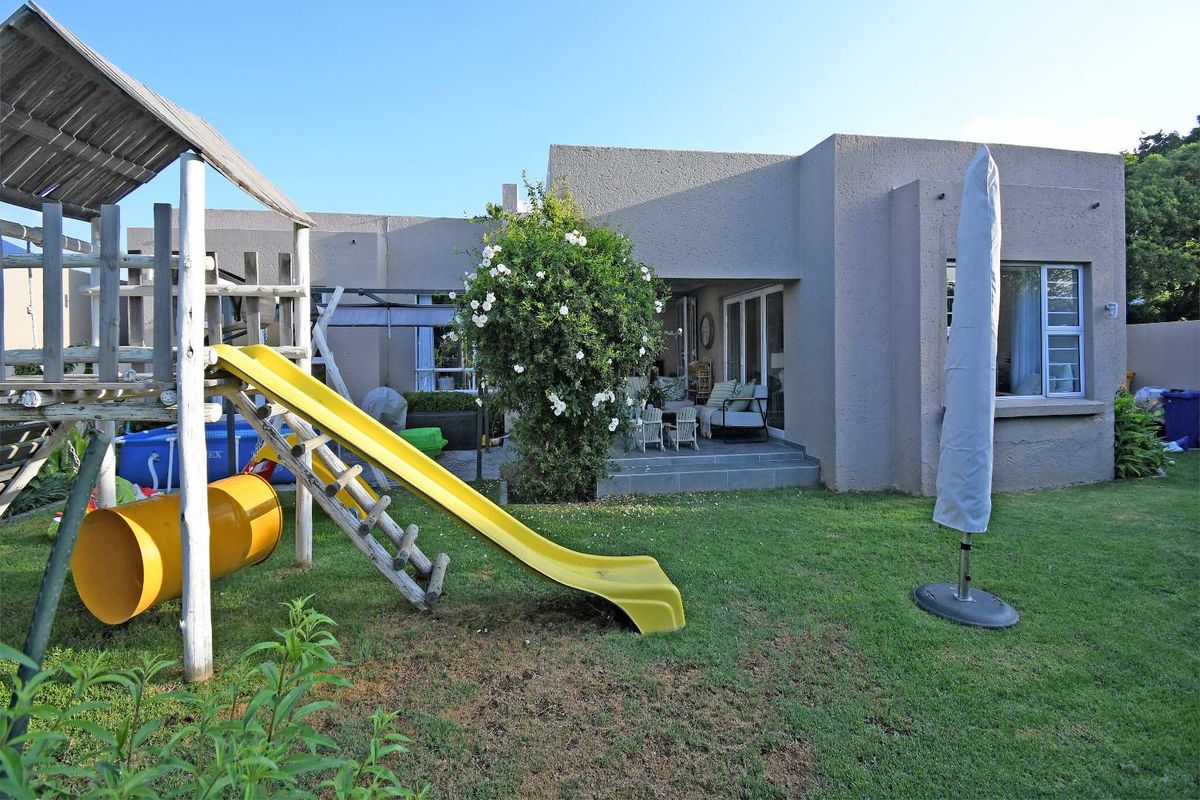 Rear view of the townhouse featuring a paved patio area, landscaped garden, and direct access to the living space through sliding glass doors.