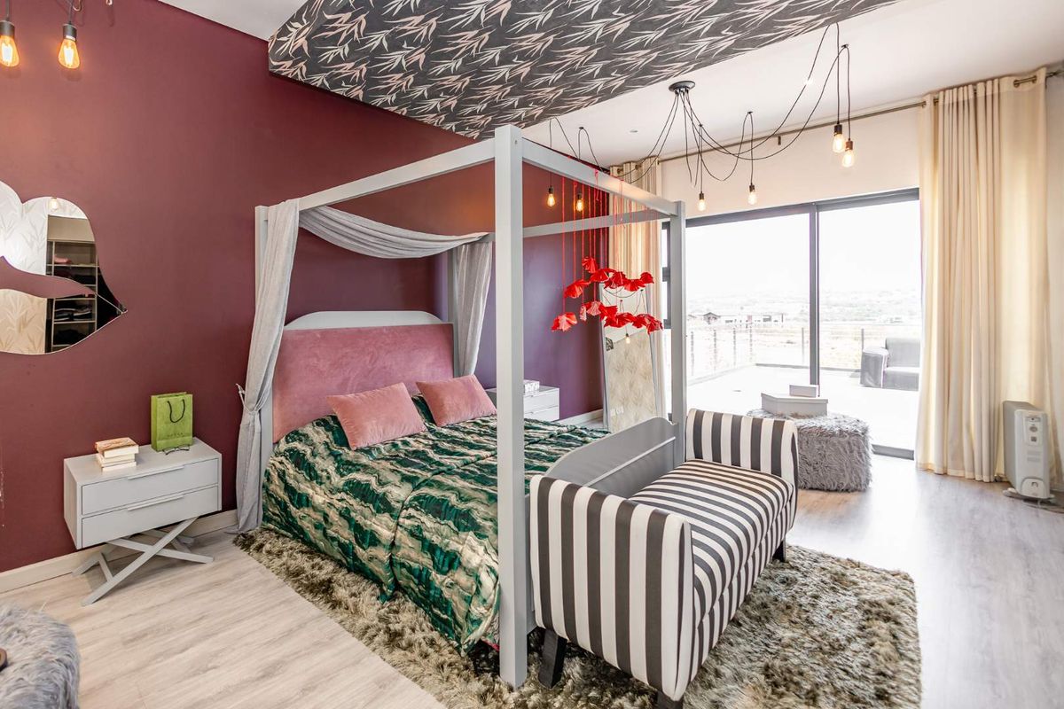 Spacious bedroom featuring modern laminate flooring, a bold accent wall, patterned ceiling detail, and large sliding glass doors providing access to an outdoor balcony.