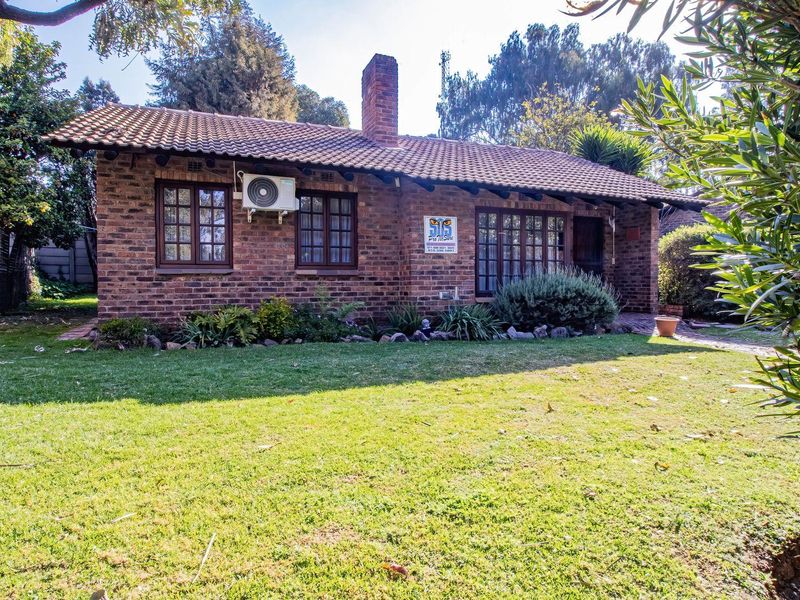 A charming face-brick townhouse exterior featuring a tiled roof, brick chimney, and established front garden with mature trees.