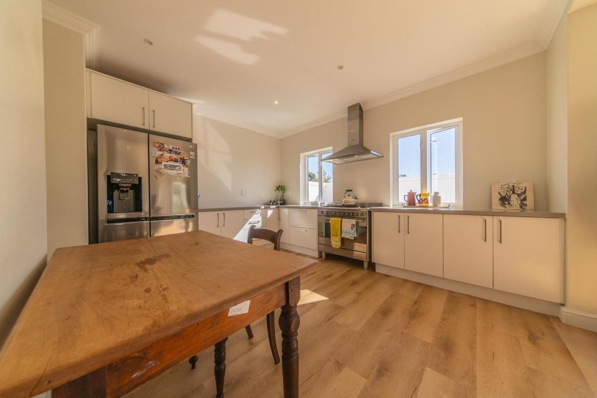 A bright, modern kitchen featuring light-toned cabinetry, stainless steel appliances, a built-in extractor fan, and durable wood-look flooring.