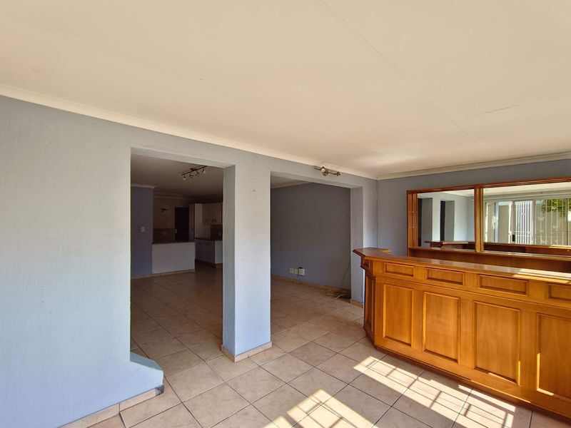 Spacious open-plan living area featuring a built-in wooden bar, ceramic tiled flooring, and a mirrored wall panel, offering a versatile layout for entertaining.