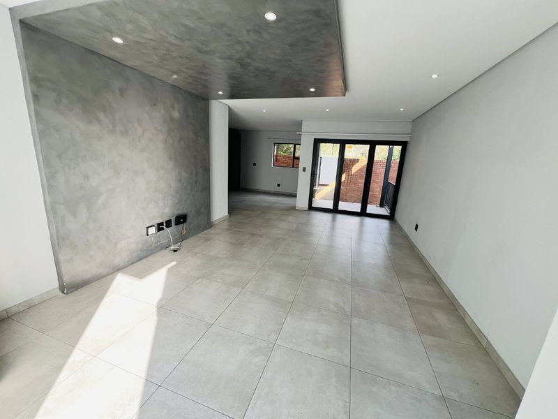 Spacious open-plan living area featuring large format floor tiles, a modern textured feature wall, recessed lighting, and sliding doors leading to the exterior.