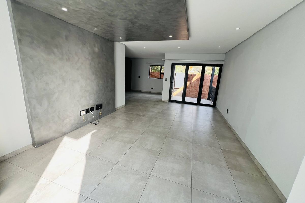 Spacious open-plan living area featuring large format floor tiles, a modern textured feature wall, recessed lighting, and sliding doors leading to the exterior.