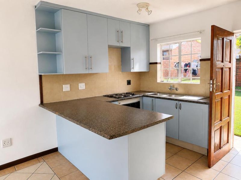 A functional kitchen featuring light blue cabinetry, a dark laminate countertop, built-in hob and oven, and tiled flooring with direct access to the exterior.