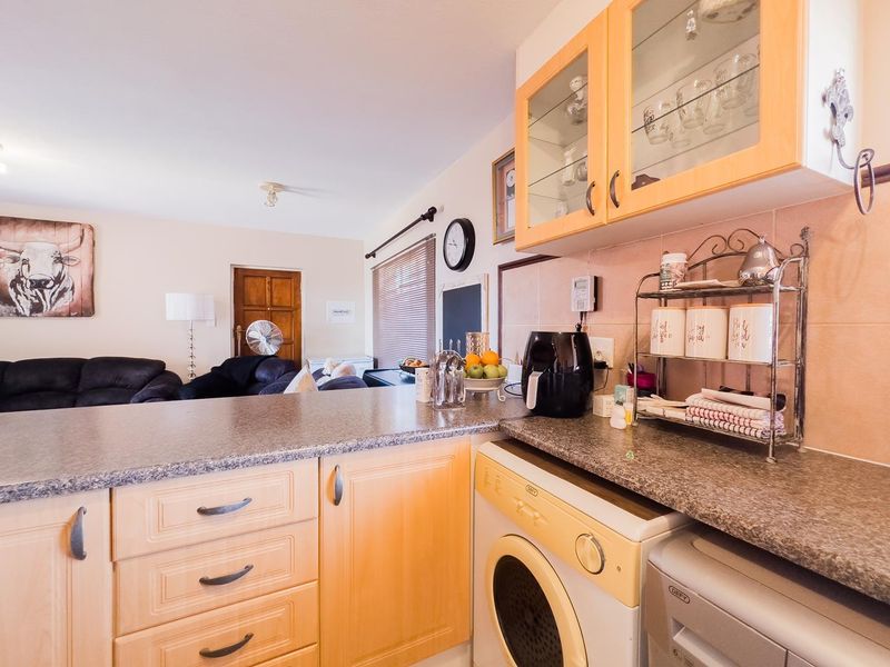 Open-plan kitchen area featuring light wood cabinetry, laminate countertops, and integrated laundry appliances, flowing into the adjacent living space.