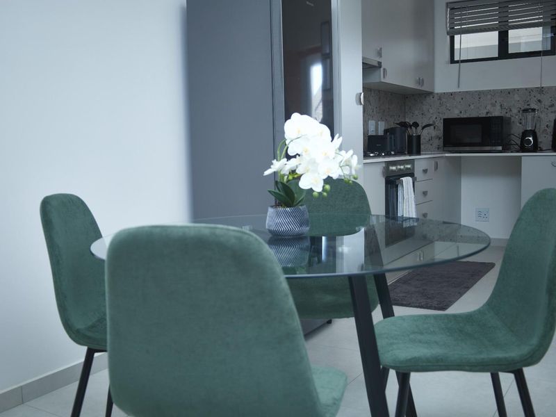 Modern open-plan kitchen and dining area featuring sleek cabinetry, a terrazzo-style backsplash, and integrated cooking appliances with neutral tiled flooring.