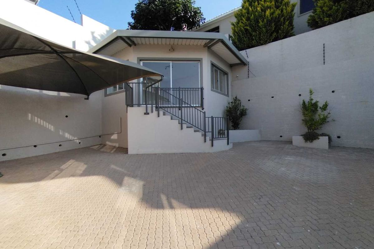 Rear exterior view featuring a paved courtyard, retaining walls, and a raised entrance with metal staircase and railing.
