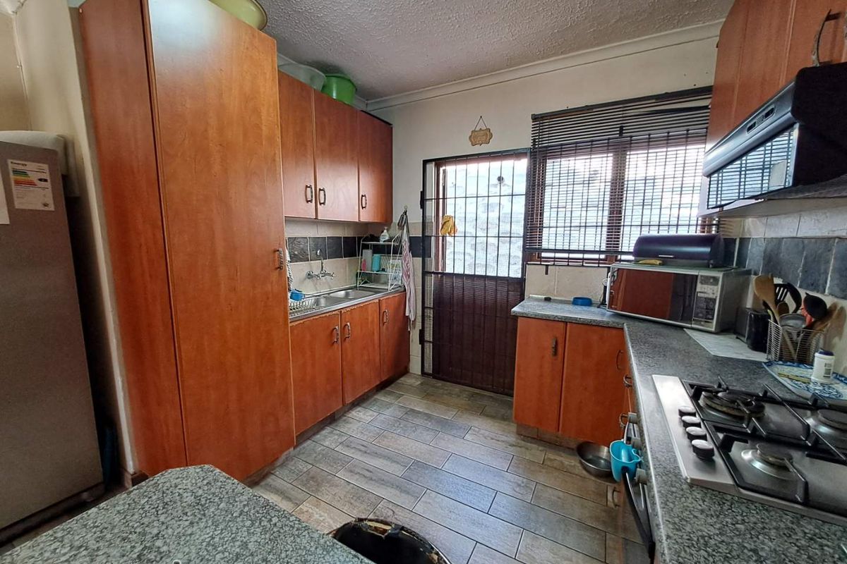 Functional kitchen featuring wood-look cabinetry, granite-style countertops, a built-in gas hob, and tiled flooring with direct access to the exterior.
