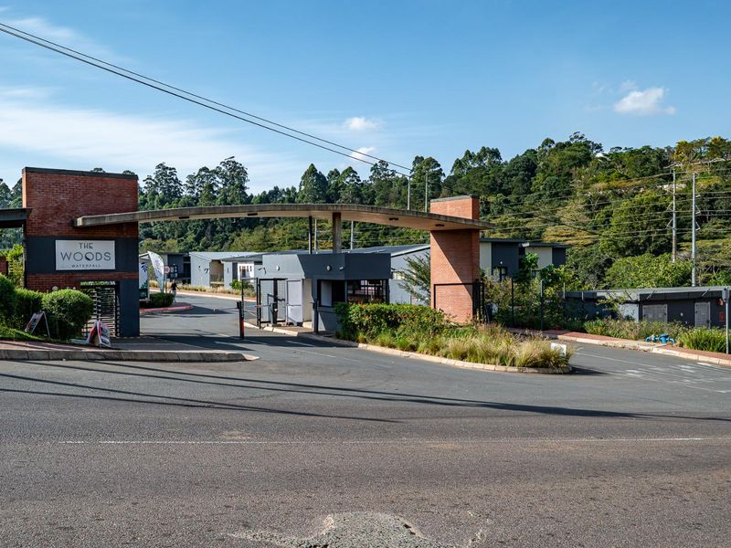 The entrance to The Woods Waterfall estate, featuring a modern brick security gatehouse, boom gate access, and well-maintained landscaped surroundings.