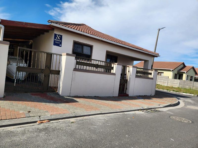 Front exterior view of a residential house featuring a tiled roof, perimeter wall with security gate, and a paved carport area.
