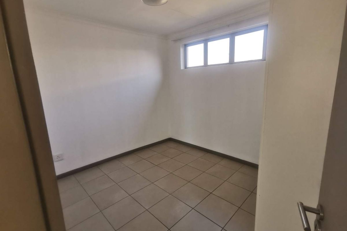 A clean, empty bedroom featuring neutral floor tiles, white walls, and a high-set window providing natural light.