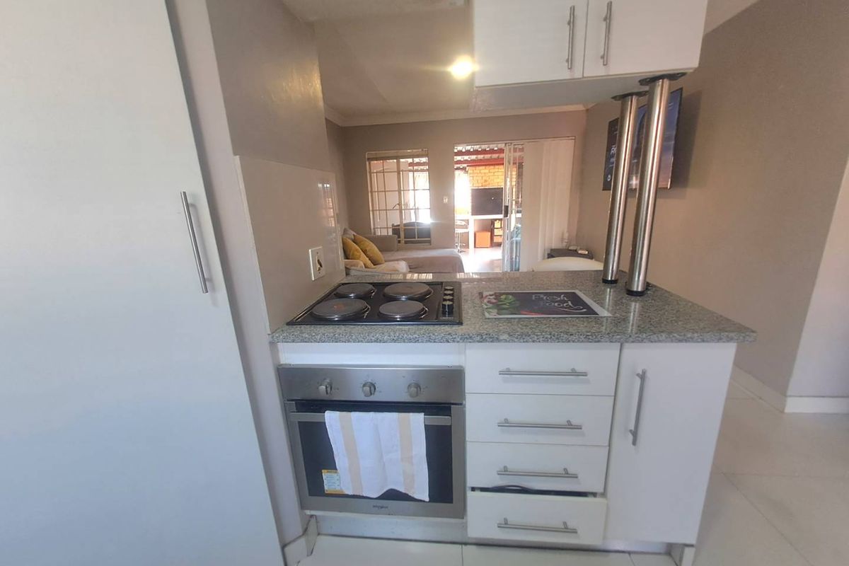 Compact kitchen featuring white cabinetry, granite countertops, a built-in oven, and an electric hob, with an open-plan layout overlooking the living area.
